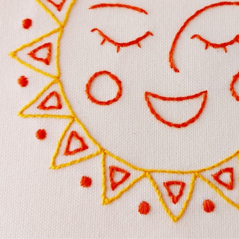 Il disegno del sole felice è ricamato a mano su una tela di cotone bianca.