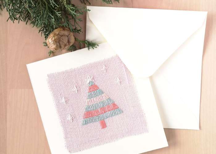 Cartolina con ricamo di albero di Natale su lino rosa, busta bianca e pigna