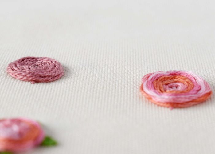Fiori rosa ricamati a mano con punto ruota intrecciato su tessuto bianco